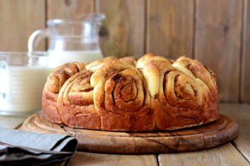 Beautiful yeast cake with cinnamon on a wooden platter close-up, a jug of milk and a glass of milk in the background