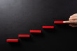 Concept of building success foundation. Women hand put red wooden block in the shape of a staircase. Success in business growth concept on black background.
