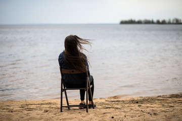 lonely girl sitting on a chair on the banks of a river or lake in silence, perfect for a poster, poster or book cover, calm mood, sad and gray
