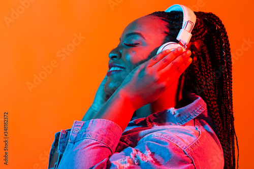 Cuadros en Lienzo Neon portrait of young african woman listening music with earphones