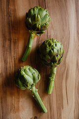 Wall Mural - Fresh green Italian Artichoke natural wood background. Organic local produce vegetable on textured table. Vegan diet. Clean eating concept. Close up, top view, flat lay.