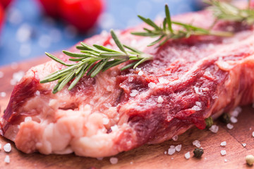 Raw meat. A large piece of beef chop on a wooden cutting board with rosemary and spices, close-up.