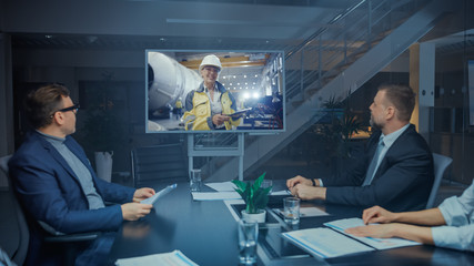 Wall Mural - Late at Night In Corporate Meeting Room: Board of Directors, Executives and Businesspeople Sitting at Negotiations Table, Having Video Conference Call with Professional Female Industrial Engineer