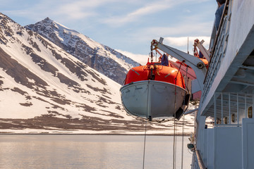 Lowering orange lifeboat to water in Arctic waters, Svalbard. Abandon ship drill. Lifeboat training. Man over board drill.