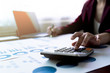 © Pravinrus - Business Woman or accountant using calculator for calculation and writing to notebook with finance report, tax document, profit loss account on table business office workplace. Business concept.