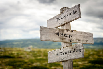 never stop dreaming text engraved on old wooden signpost outdoors in nature. Quotes, words and illustration concept.