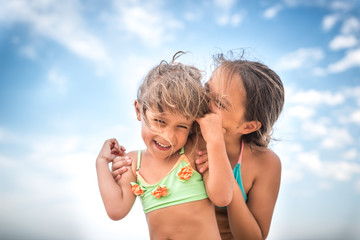 Little charming sisters whispers something in each other s ear during summer vacation on a warm summer day against a blue sky. Concept of healthy children resting. Copyspace