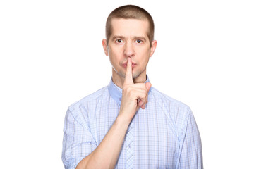 Wall Mural - Serious man in a classic blue shirt; shows a gesture of silence, the preservation of silence and mystery; put his index finger to his lips; look into the camera. Isolated