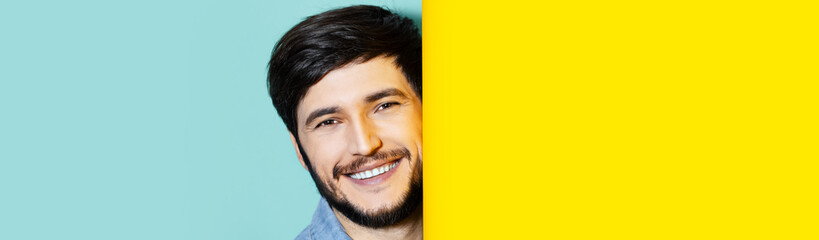 Studio portrait of young smiling guy between two backgrounds of yellow and aqua menthe colors.