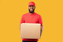 Smiling Courier Offering Cardboard Box To Camera Over Yellow Background