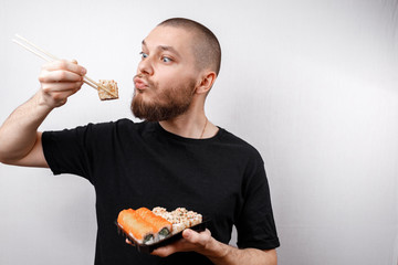 young man in a black T-shirt eats sushi rolls