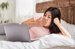 © Prostock-studio - Bored Asian Girl Using Laptop Lying In Bed At Home