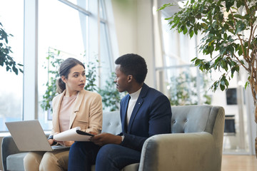 Wall Mural - portrait of successful african businessman talking to female partner while working sitting comfortab