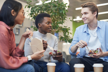 Wall Mural - multi-ethnic group of young people eating takeout food and smiling during lunch break in school or o