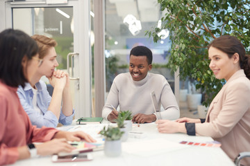 Wall Mural - Multi-ethnic group of young business people collaborating on work project during meeting in office, focus on smiling African-American man heading table
