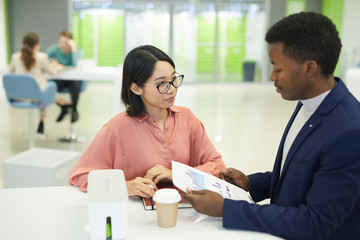 Wall Mural - Portrait young Asian businesswoman discussing work documents with colleague while sitting at table during lunch break in office