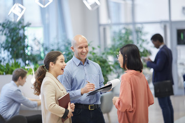 Wall Mural - Waist up view at group of three business people laughing happily while standing in modern office interior, copy space