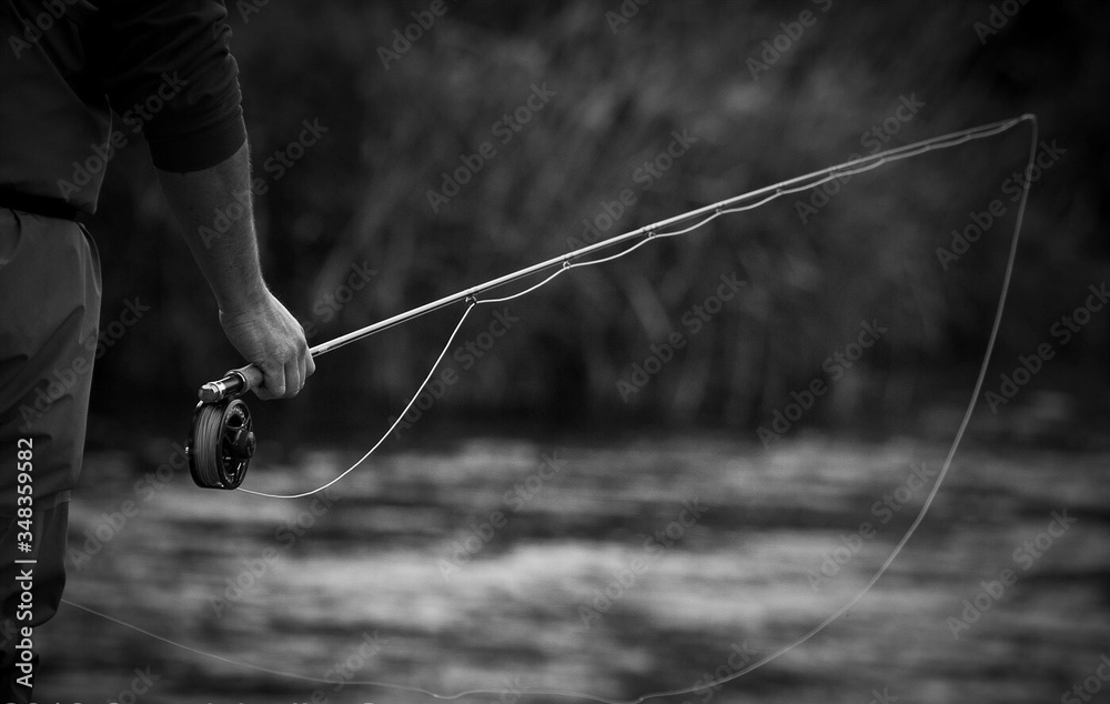 Close-up Of Man Holding Fishing Rod By River - obrazy, fototapety, plakaty 