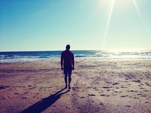 Rear View Of Man Walking On Beach Against Clear Sky