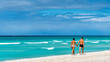 © Daniel Avram - An elegant traveler couple walks down a tropical beach with coconut palm trees and turquoise waters on a tropical island.