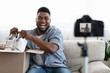 © Prostock-studio - Joyful Black Man Blogger Recording Unboxing Video Of New Pair Of Shoes