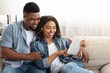 © Prostock-studio - Positive African Couple Relaxing With Digital Tablet At Home, Sharing Earphones