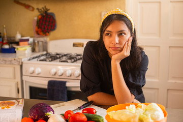 Hispanic woman thinking in the kitchen - young woman standing in the kitchen with vegetables on the table - healthy food - vegetarian food - recipes at home