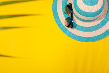 Wall Mural - Top view on beach accessories on yellow background - sunglasses and striped blue hat in palm leaf shadow. Concept of beach holiday, sea tour, warm sunny summer. Advertising space