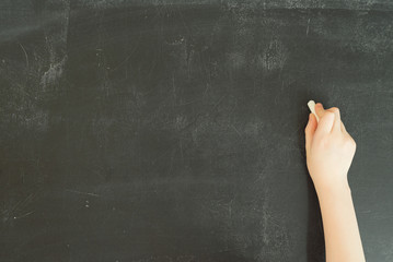 child's hand holding white chalk to writing or drawing on black chalkboard, stock photo image template with copy space on blackboard background