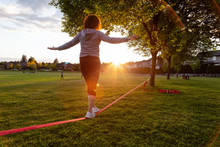 Girl Walking On A Slackline In A Park During A Sunny Sunset. Taken In Fraser Heights, Surrey, Greater Vancouver, British Columbia, Canada.