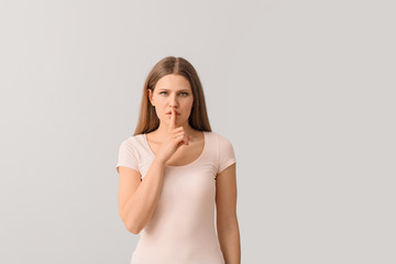 Canvas Print - Young woman showing silence gesture on light background