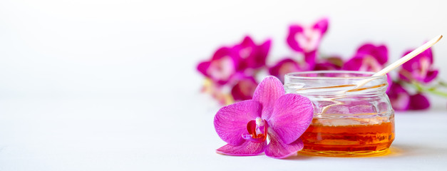 banner depilation and beauty - sugar paste or wax honey for hair removing with wooden waxing spatula stick in jar on flower background. copyspace