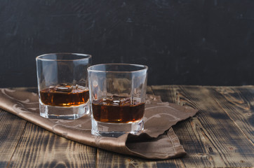 Wall Mural - Two Glasses of whiskey with ice cubes on a wooden table/Two Glasses of whiskey with ice cubes on a wooden table. Black background with copyspace.