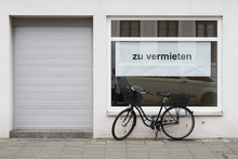 German Vacancy Sign In Store Window - Zu Vermieten Translates As For Rent Or To Let - Bicycle Parked Outside Closed Shop