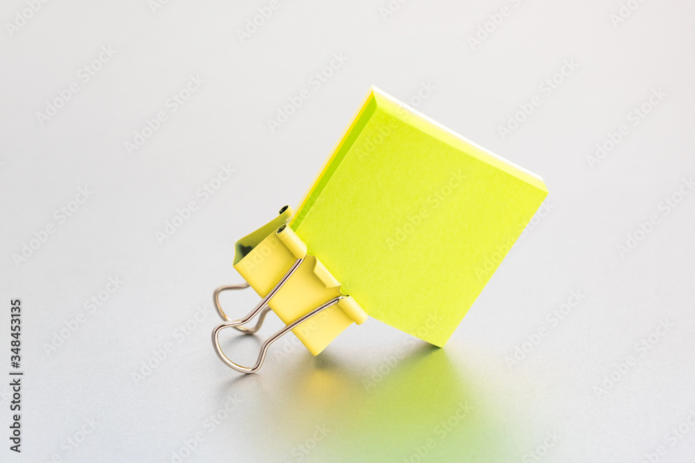 Yellow paper clip on clean color paper blok - a cover on a silver grey background - obrazy, fototapety, plakaty 