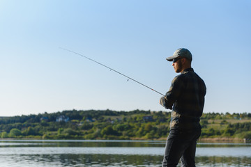 Wall Mural - Fishing for pike, perch, carp. Fisherman with rod, spinning reel on river bank. Man catching fish, pulling rod while fishing on lake, pond with text space. Wild nature. The concept of rural getaway.