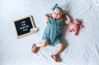 10 Ten months old baby girl laying down on white background with letter board and teddy bear. Flat lay composition.