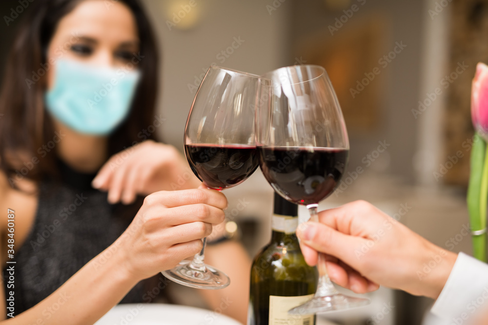 Masked couple toasting wineglasses in a restaurant during coronavirus pandemic - obrazy, fototapety, plakaty 