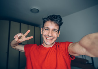 Happy young man takes selfie portrait at home indoor. Guy smiling looking at the camera.