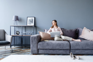 Beautiful self-confident positive healthy young woman designer working on her company website sitting in comfortable living room with laptop and high-speed internet. Remote work at home concept