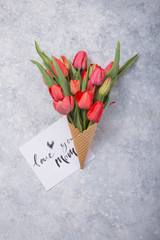 Wall Mural - Ice cream of red  tulip flowers in waffle cone with card Love you mom  on concrete  table top view in flat lay style.