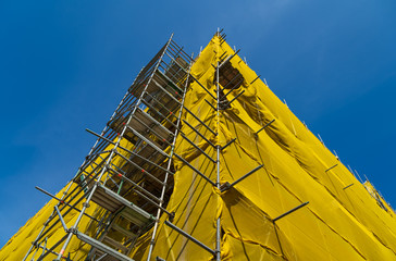 Fototapeta A constuction-site with a building in scaffolding and yellow mesh.