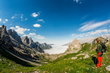 Wall Mural - hiker observing the tall meadows at his feet and the sea of ​​clouds in the background over the valley
