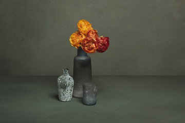 Vintage vase with red and orange peony tulips and two empty little vases in a grey room.