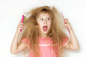 a little girl with tangled long hair in a pink dress on a white background. stands with two combs in different hands and does not know what to do