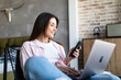 © F8  \ Suport Ukraine - Portrait of smiling young beautiful woman talking on smartphone, working on laptop and sitting on chair at home