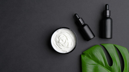 Set of luxury natural skin care products on black background. Flat lay, top view organic herbal cream and lotion with tropical leaf.