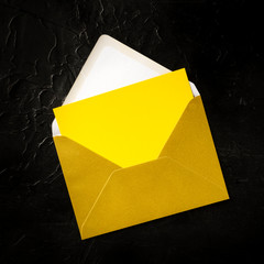 Wall Mural - A yellow greeting card in a golden envelope mock-up, overhead square shot on a dark background with copy space