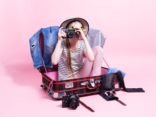 Travel: A schoolgirl girl is preparing for a trip, sitting in a large suitcase with things and holding a large retoro camera in her hands.