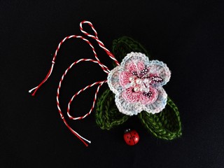 Handmade crocheted flower on black background and red and white string, known as Martisor. It is a Romanian traditional symbol of the beginning of spring.
